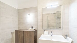 Ein modernes Badezimmer mit Holzschrank, weißem Waschbecken und einer Duschkabine aus Glas.