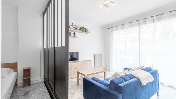 Ein modernes Wohnzimmer mit einem blauen Sofa, einem Fernseher, einem Holztisch und einer Pflanze auf einem Regal.