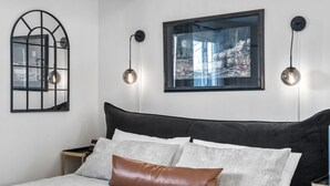 A neatly arranged bedroom with a large bed, two bedside tables, a wall-mounted picture, and two wall-mounted lamps. - Beach Cottage 1-Block to Ocean! (Wildwood)