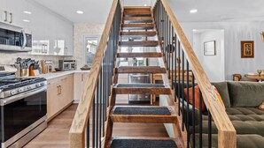 A modern kitchen with a wooden staircase, stainless steel appliances, and a green sofa in the living area. - Beach Cottage 1-Block to Ocean! (Wildwood)