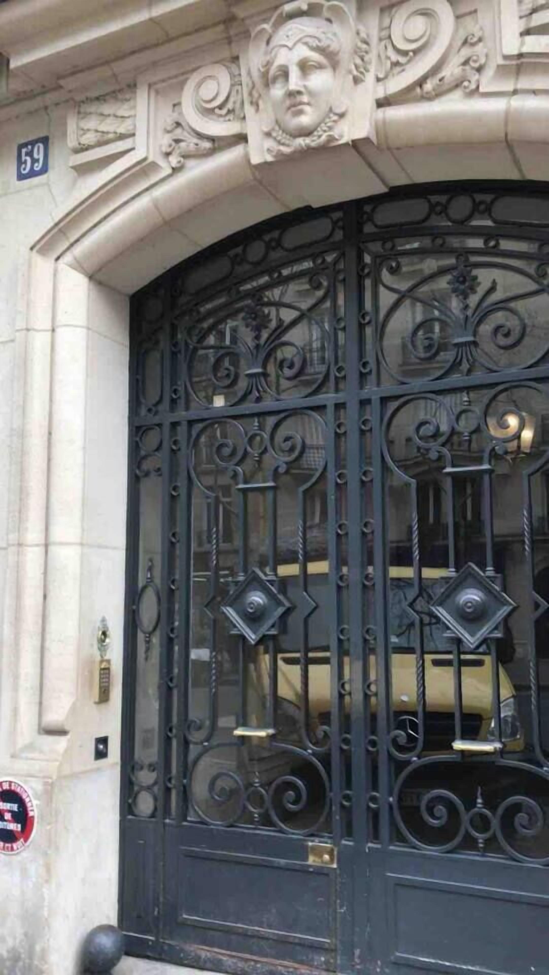 Un portail en fer forgé noir, agrémenté d’éléments décoratifs, avec une plaque portant le numéro « 59 » au-dessus.