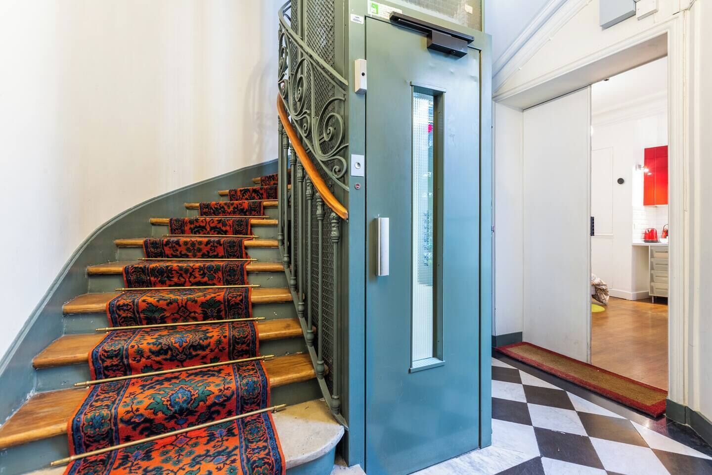 A staircase with ornate metal railings and patterned carpet runners, leading to a blue elevator.