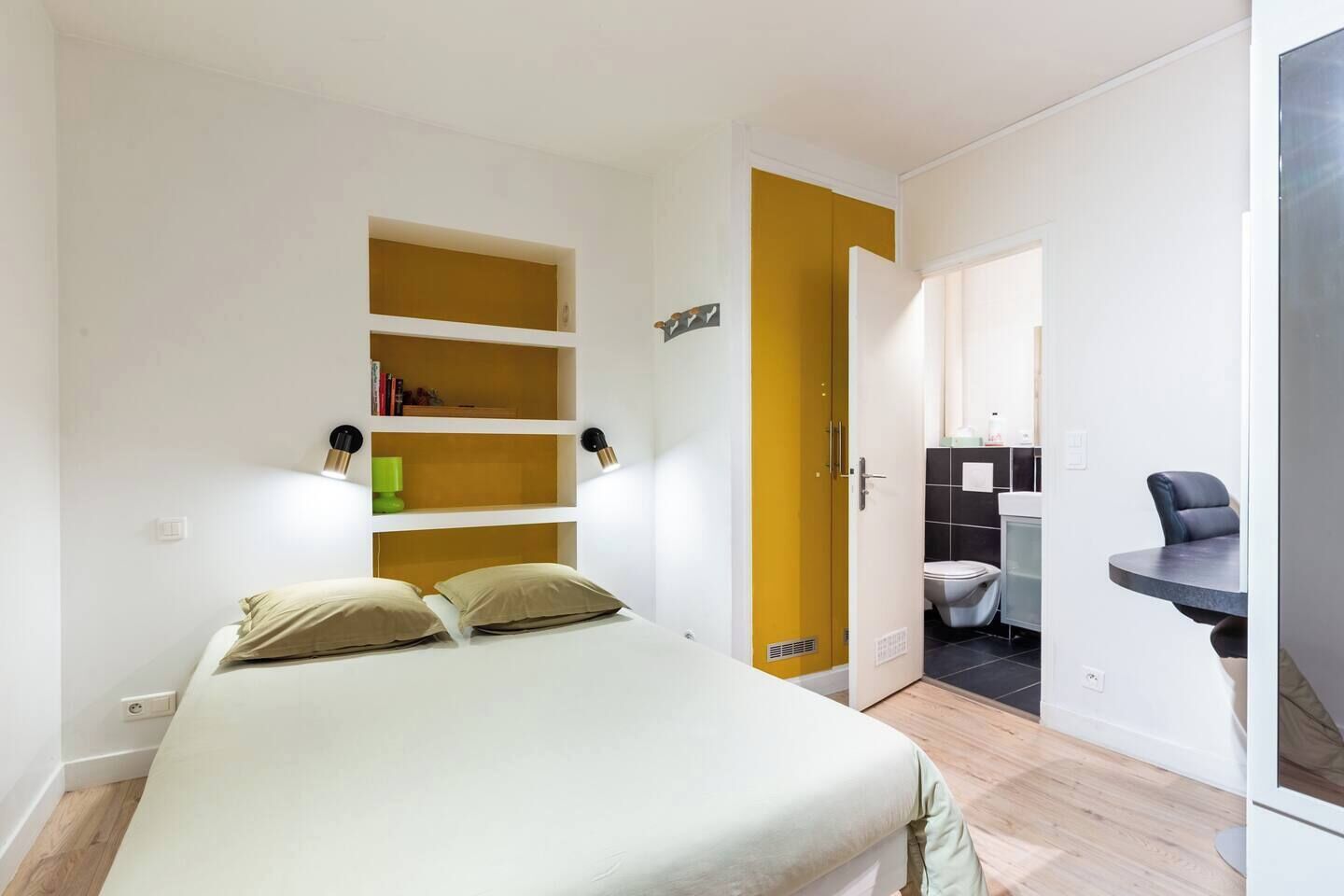 A bedroom with a bed, built-in shelves, a wardrobe, and a bathroom visible through an open door.