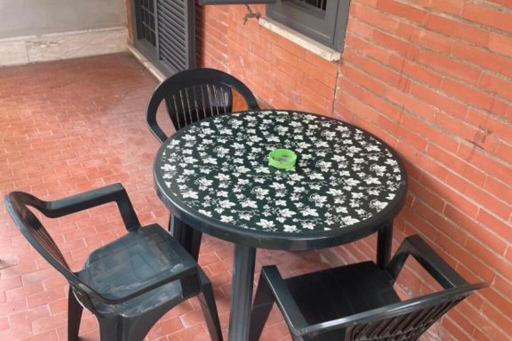 Uma mesa redonda com toalha florida, rodeada por quatro cadeiras pretas.