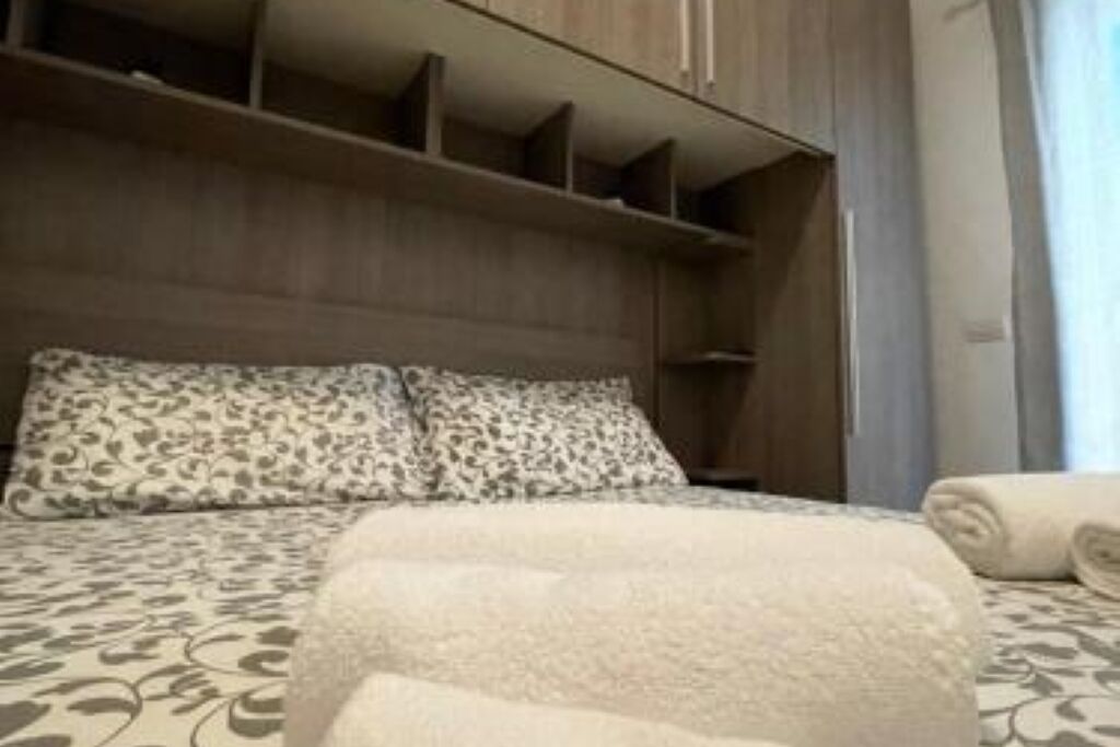 A hotel room with a bed, a headboard, a wardrobe, and a window with curtains.