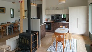 A modern kitchen with a central island, wooden chairs, a dining table, and a black wood-burning stove. - Merry Méry (Mery)
