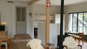 A cozy living room with wooden chairs, a sofa, a fireplace, and a kitchen area in the background. - Merry Méry (Mery)