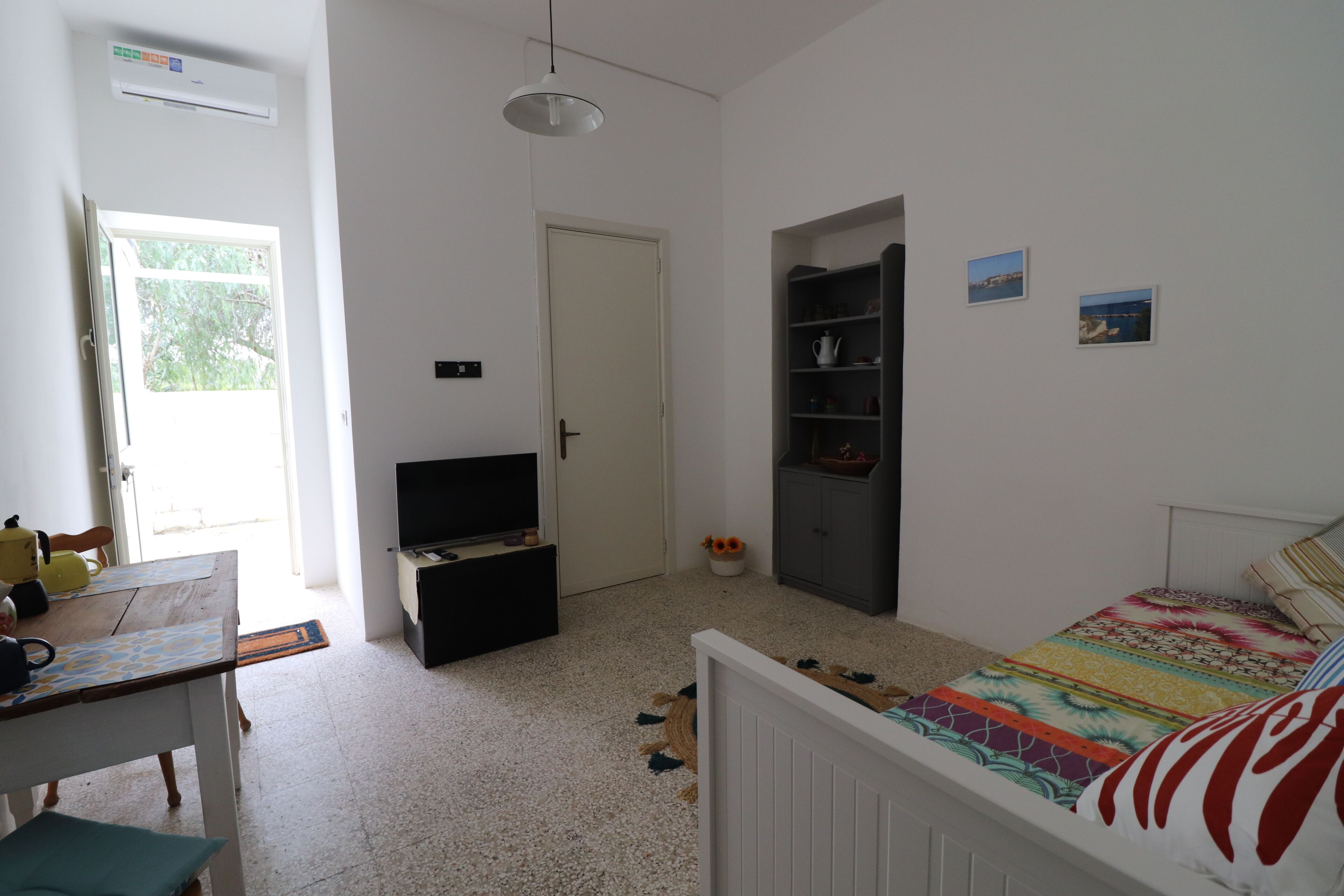 Ein Schlafzimmer mit Bett, Fernseher, Kleiderschrank und einer Tür zu einem weiteren Raum.