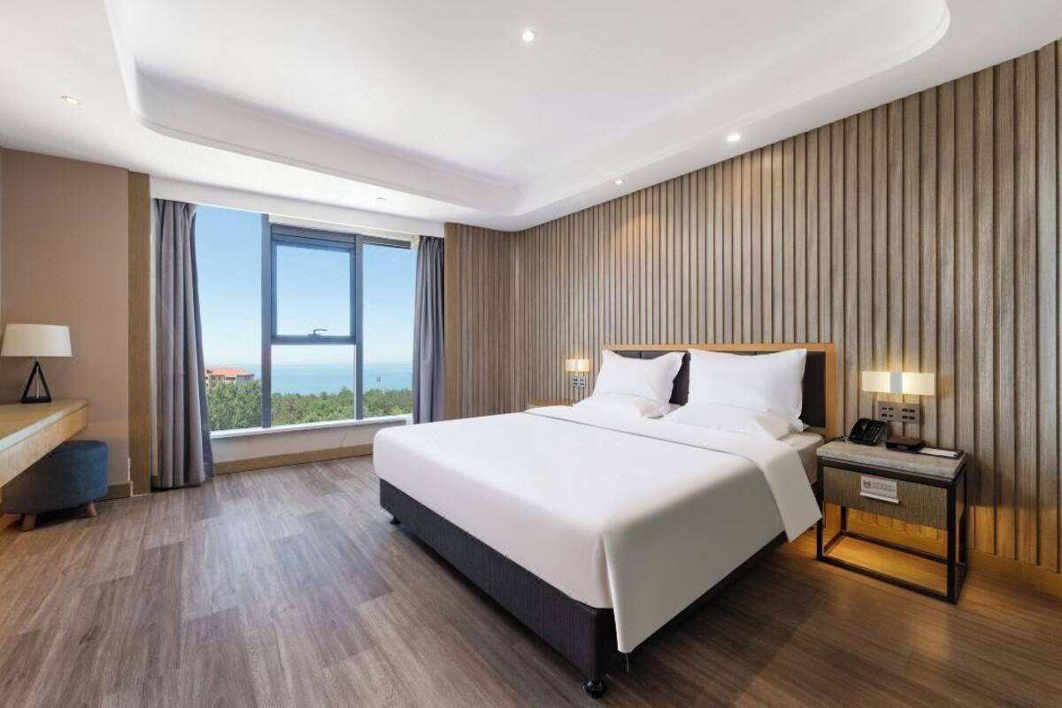A modern hotel room with a large bed, a desk, and a view of the city.