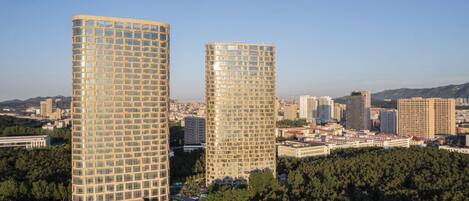A high-rise building with a grid-like facade, surrounded by a dense urban environment and greenery.