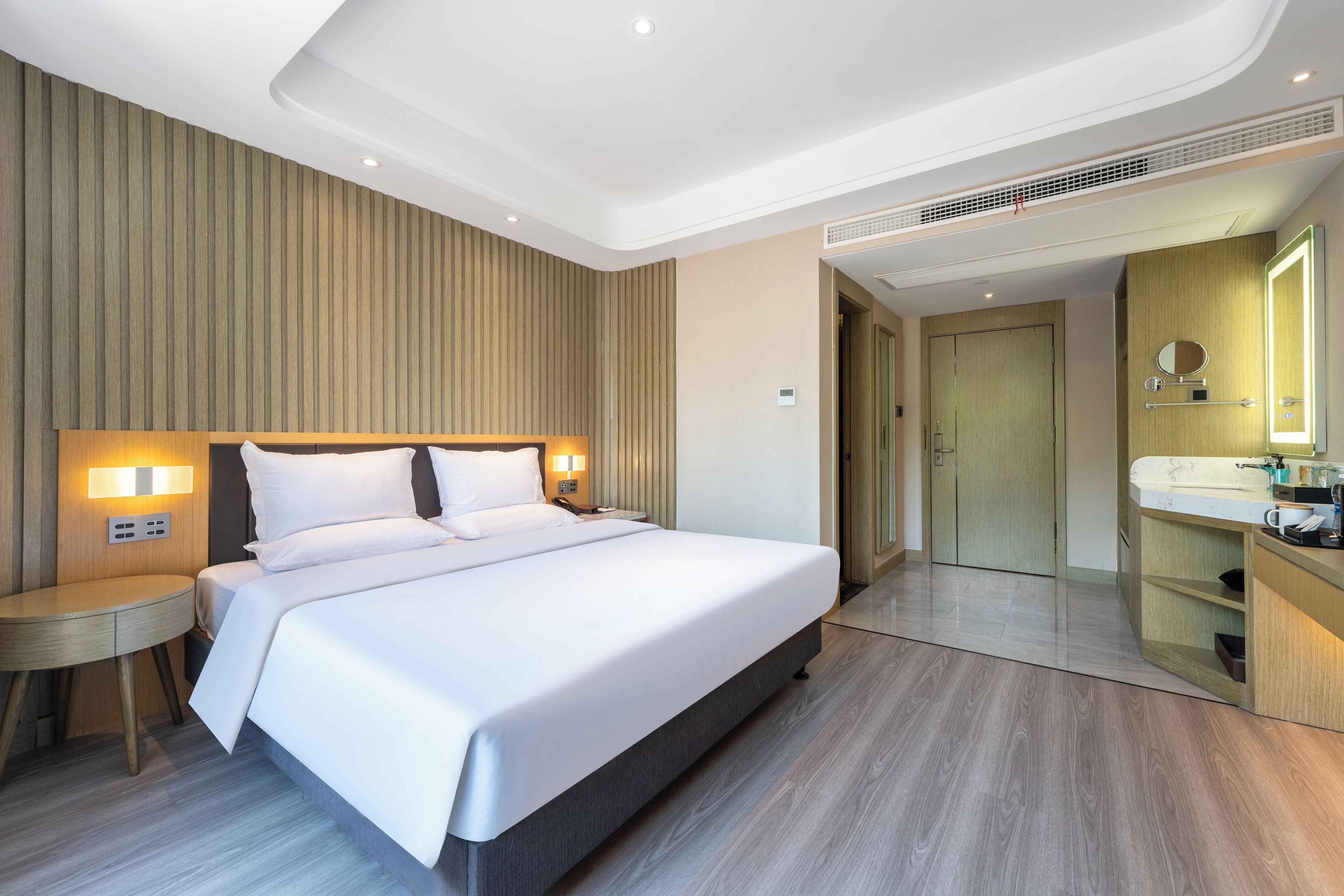 Una habitación de hotel moderna con una cama grande, mesitas de noche, un tocador empotrado con espejo y un vestidor.