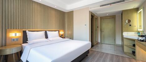 Una habitación de hotel moderna con una cama grande, mesitas de noche, un tocador empotrado con espejo y un vestidor.