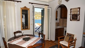 A dining area with a round table, chairs, a mirror, and a view of the sea through an open door. - Traditional island house (Andros)