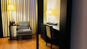 A hotel room with a checkered armchair, a desk with a lamp, and a bookshelf. - Hotel Rivo Timisoara (Timisoara)
