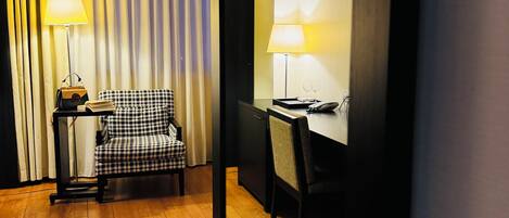 Una habitación de hotel con un sillón a cuadros, un escritorio con lámpara y una estantería.