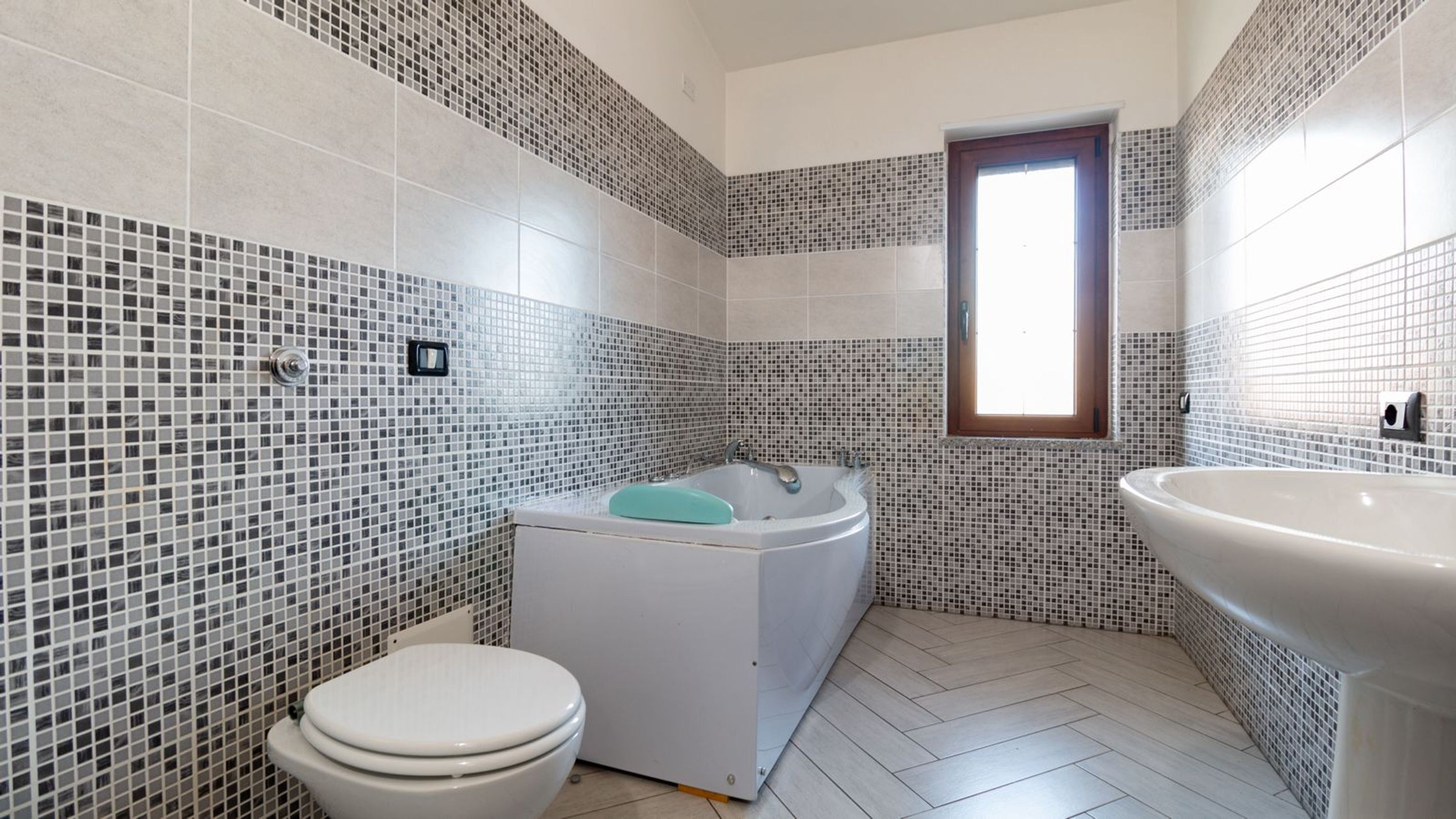 Ein Badezimmer mit Toilette, einer Badewanne mit blauer Sitzfläche und einem Waschbecken.