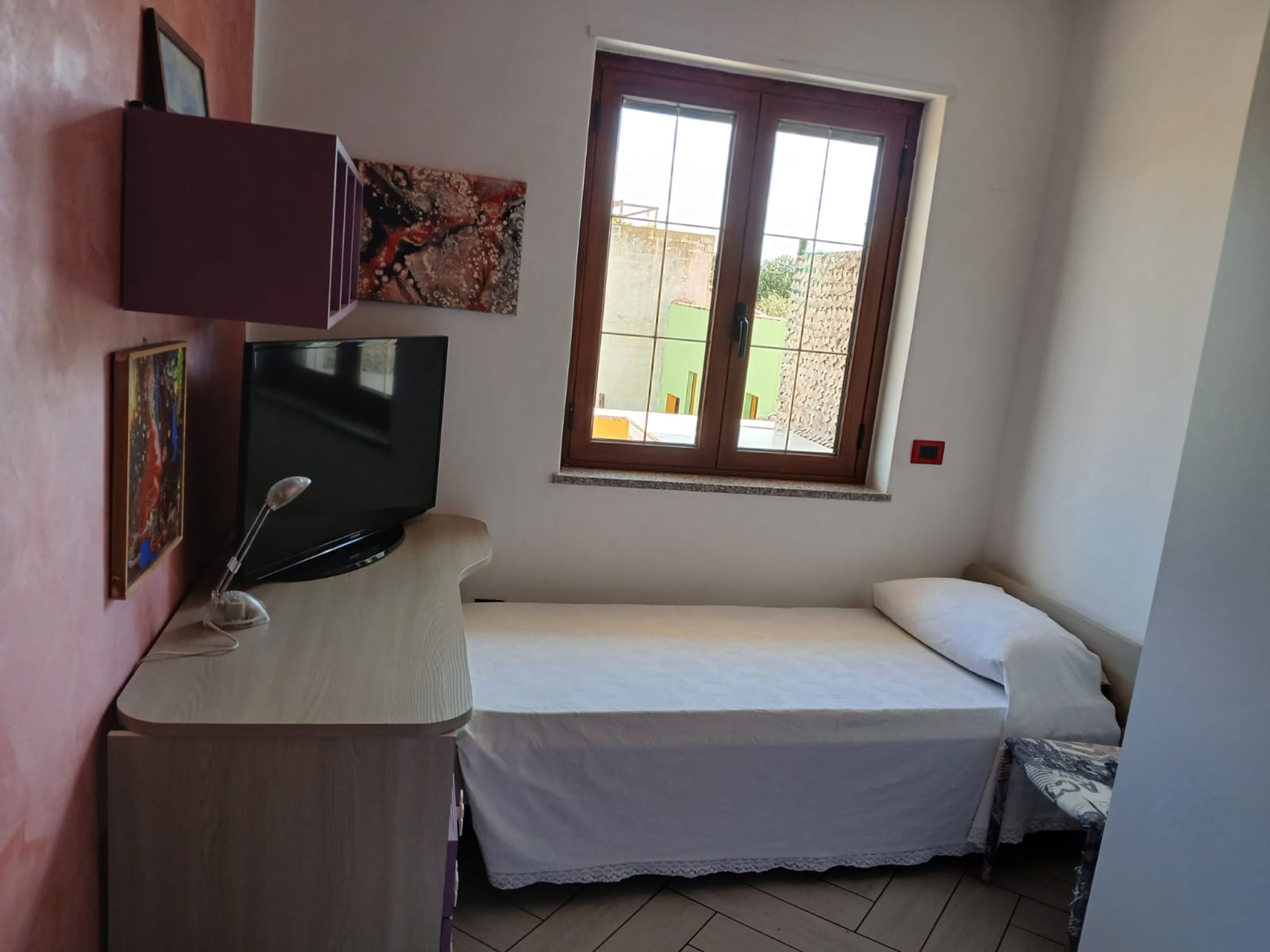 A small room with a bed, a TV, and a window.