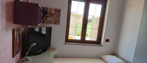 A small room with a bed, a TV, and a window.