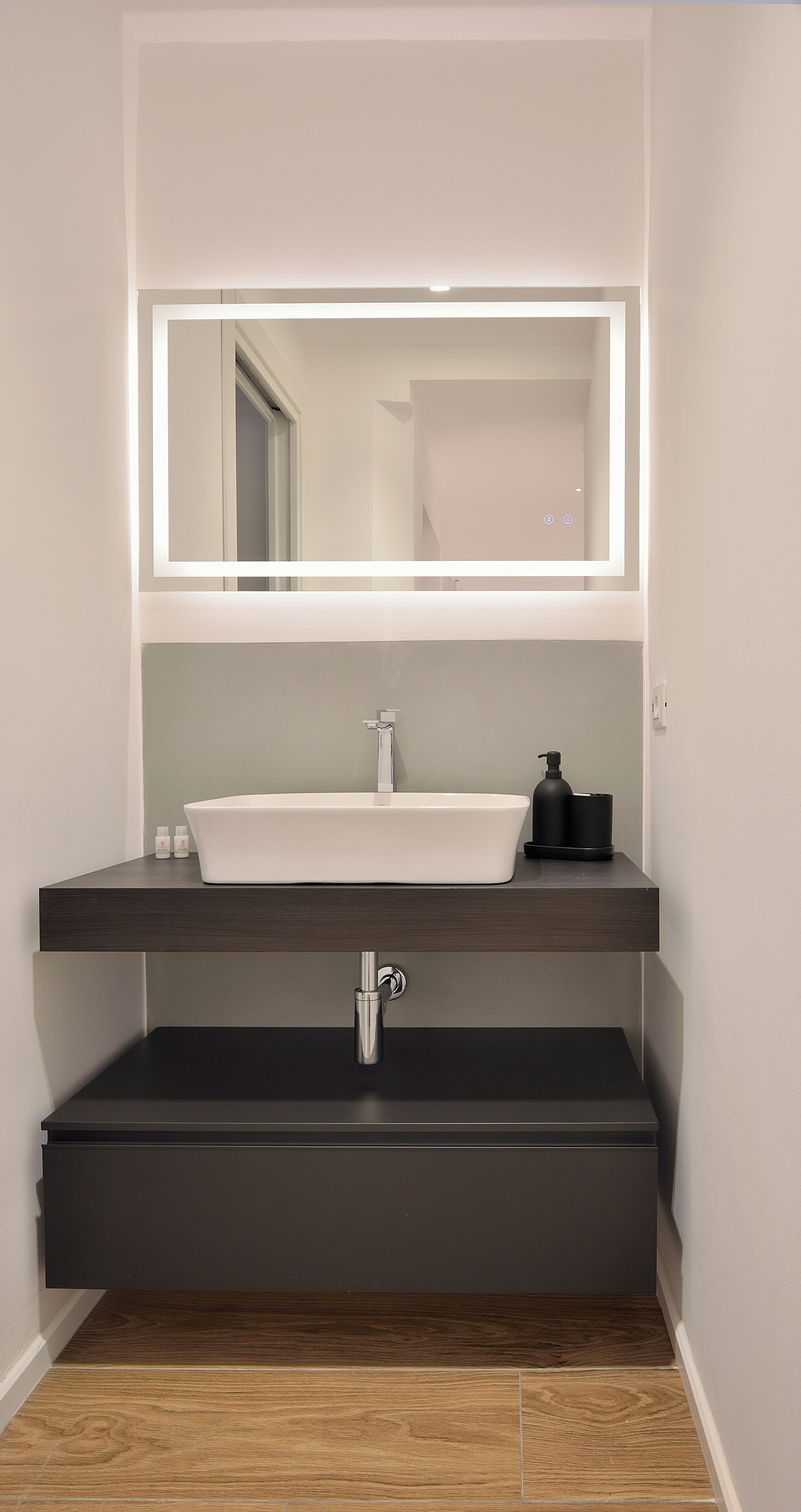 Ein modernes Badezimmer mit einem großen Spiegel, einem weißen Waschbecken und einer schwarzen Arbeitsplatte.