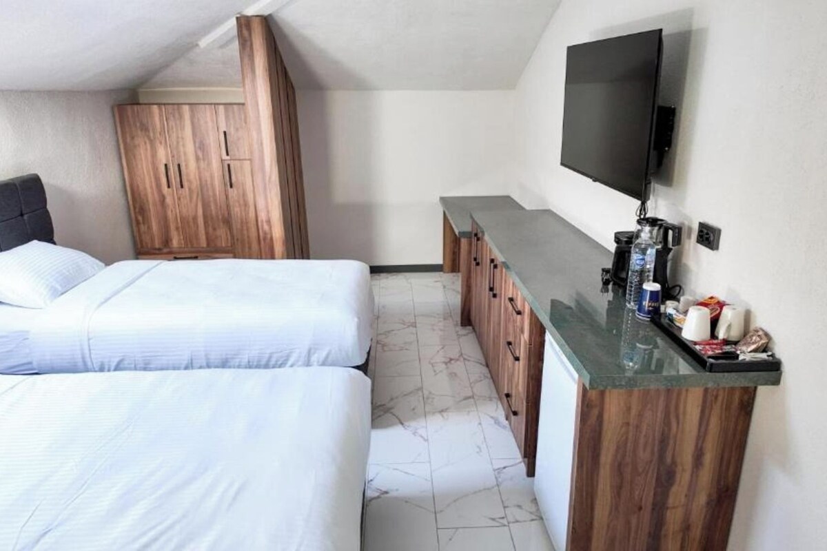 A hotel room with two beds, a wooden wardrobe, a minibar, and a TV mounted on the wall.