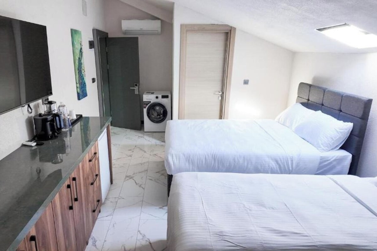 A hotel room with a bed, a TV, a washing machine, and a kitchenette.