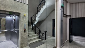 An elevator, a staircase with black railings, and a door with an exit sign. - Faraza Rooms (Serdivan)