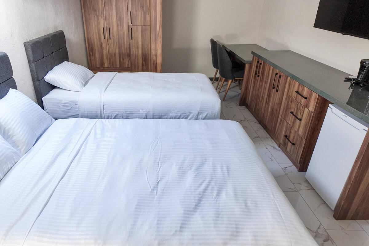 A bedroom with two beds, a wooden wardrobe, a desk, and a television.