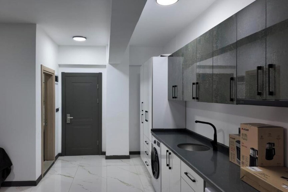 A modern kitchen with a dark countertop, white cabinets, and a washing machine.