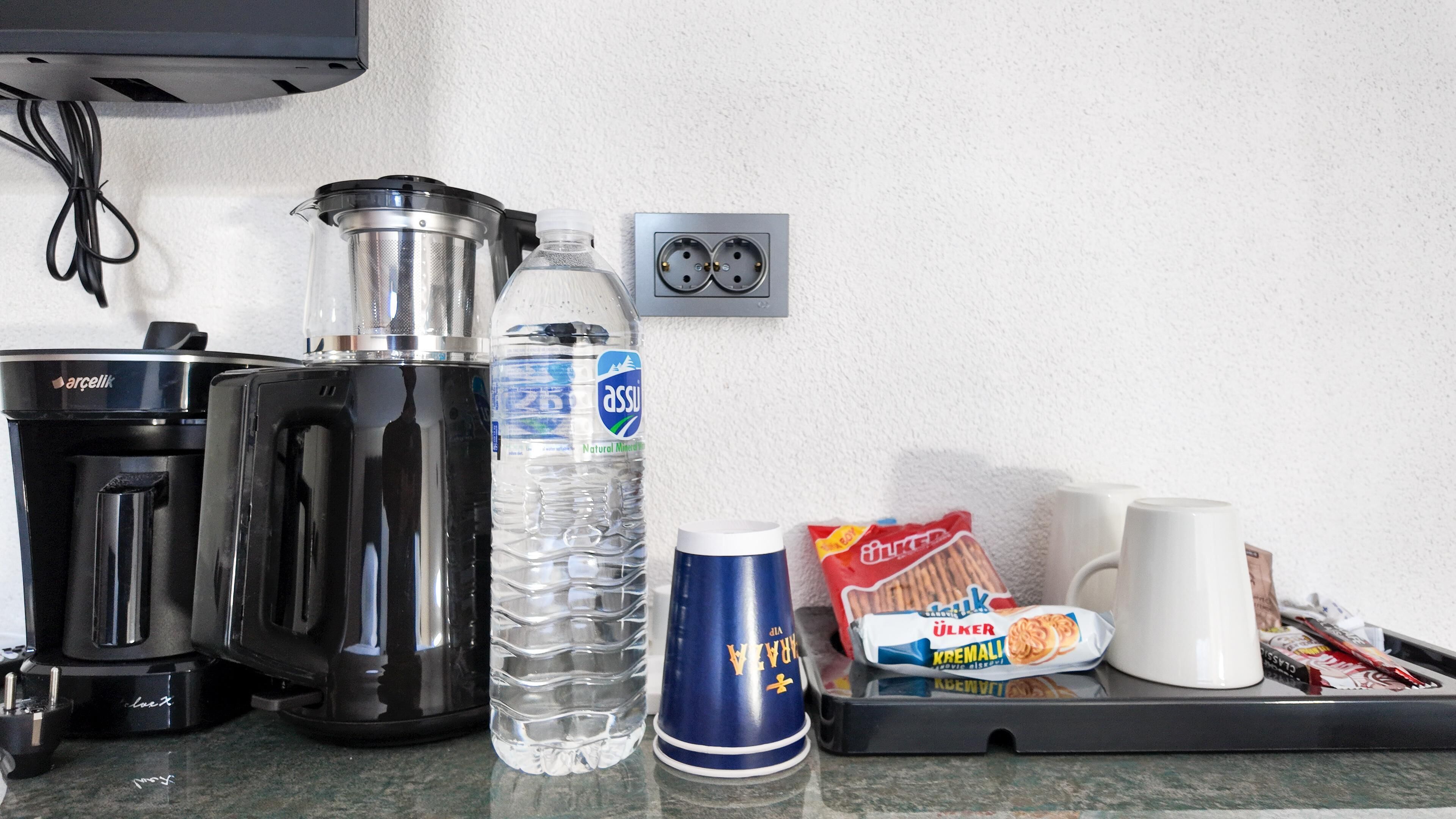 En köksbänk med en kaffebryggare, en vattenflaska, en mugg och förpackade snacks.