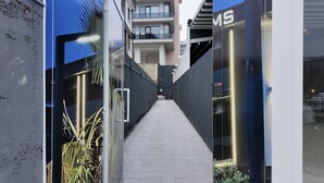A narrow corridor with a metal gate, a palm tree, and a building with balconies. - Faraza Rooms (Serdivan)