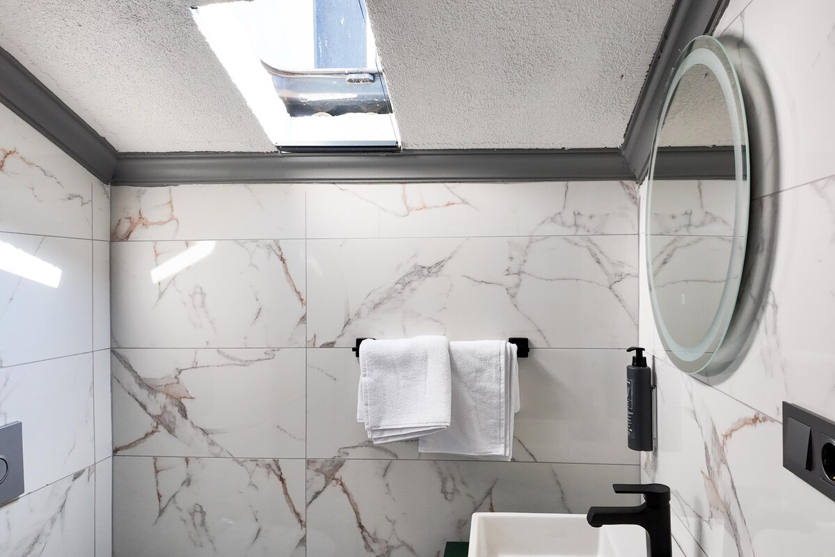 A bathroom with marble tiles, a mirror, a towel rack, and a black faucet.