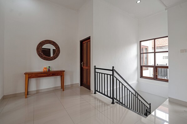 A clean, modern interior with a wooden console table, a mirror, a staircase with a black railing, and a large window. - The Light House (Ubud)