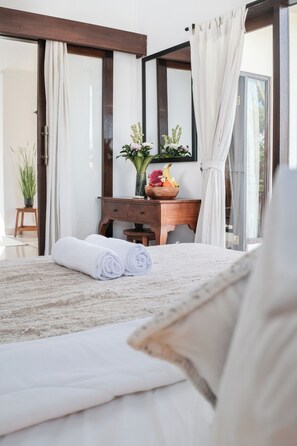 A bedroom with a bed, a wooden desk, a potted plant, and a bowl of fruit. - The Light House (Ubud)