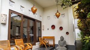 Ein ruhiger Außenbereich mit Holzbänken und -tischen, einer Buddha-Statue, dekorativen Laternen und einem kleinen Garten mit Pflanzen.