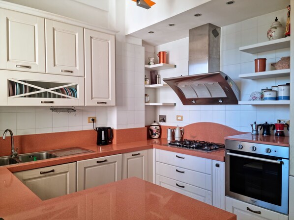 A modern kitchen with white cabinetry, a gas stove, an oven, and a coffee maker.