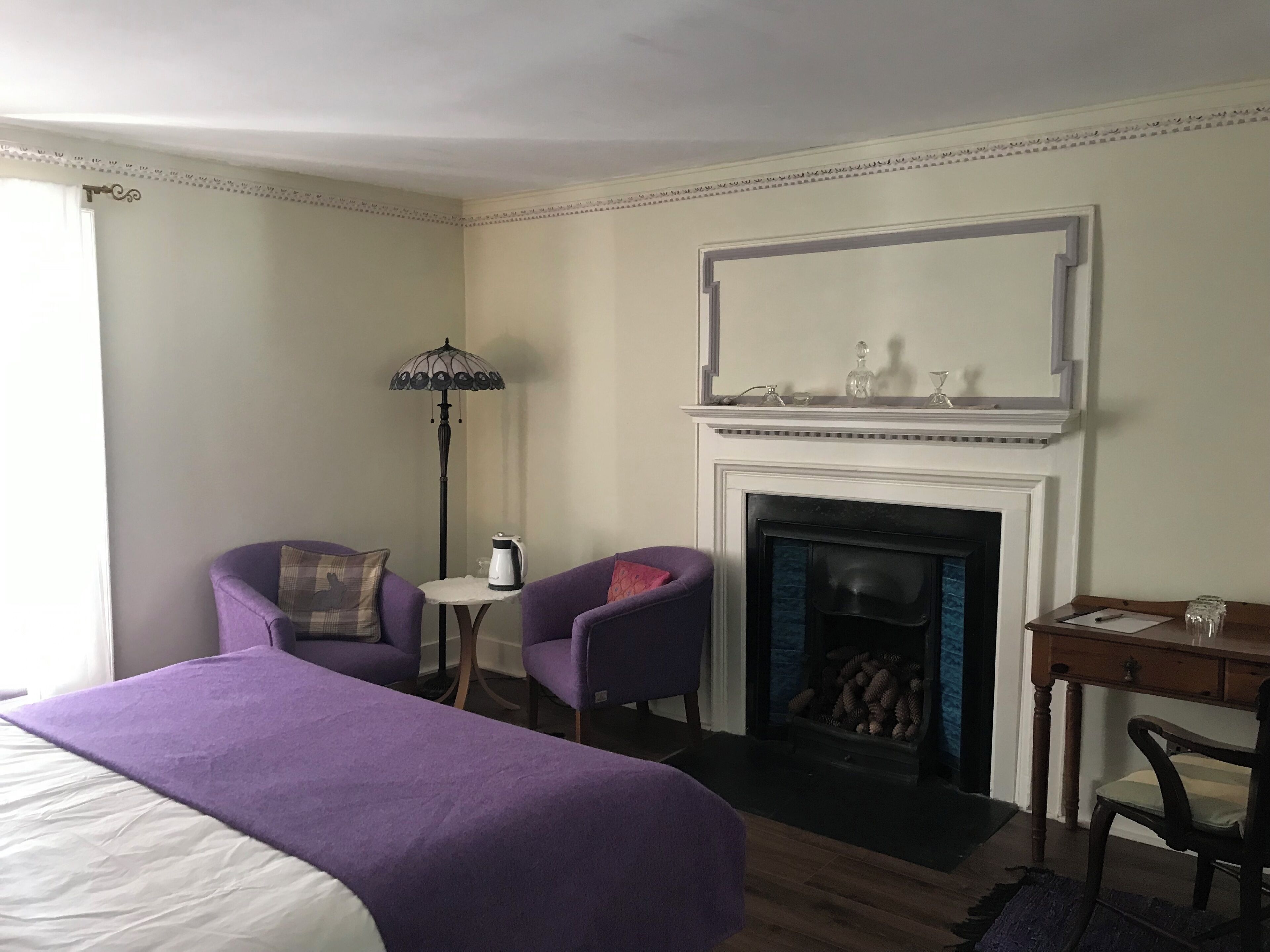 Ein Hotelzimmer mit einem großen Bett, zwei Sesseln, einem kleinen Tisch mit Wasserkocher, einem Kamin und einem Schreibtisch mit Stuhl.