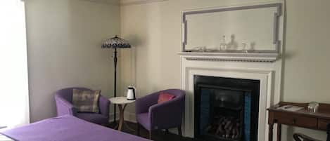 Ein Hotelzimmer mit einem großen Bett, zwei Sesseln, einem kleinen Tisch mit Wasserkocher, einem Kamin und einem Schreibtisch mit Stuhl.