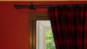 Une pièce avec un mur rouge, une fenêtre donnant sur un paysage verdoyant, un banc et un lit avec une tête de lit.