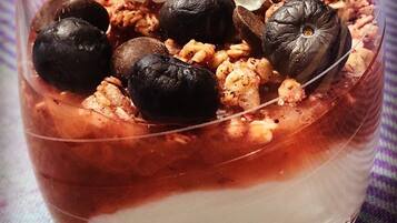 Postre en un tazón de vidrio transparente con capas de chocolate y fruta, coronado con aceitunas negras y flores blancas.