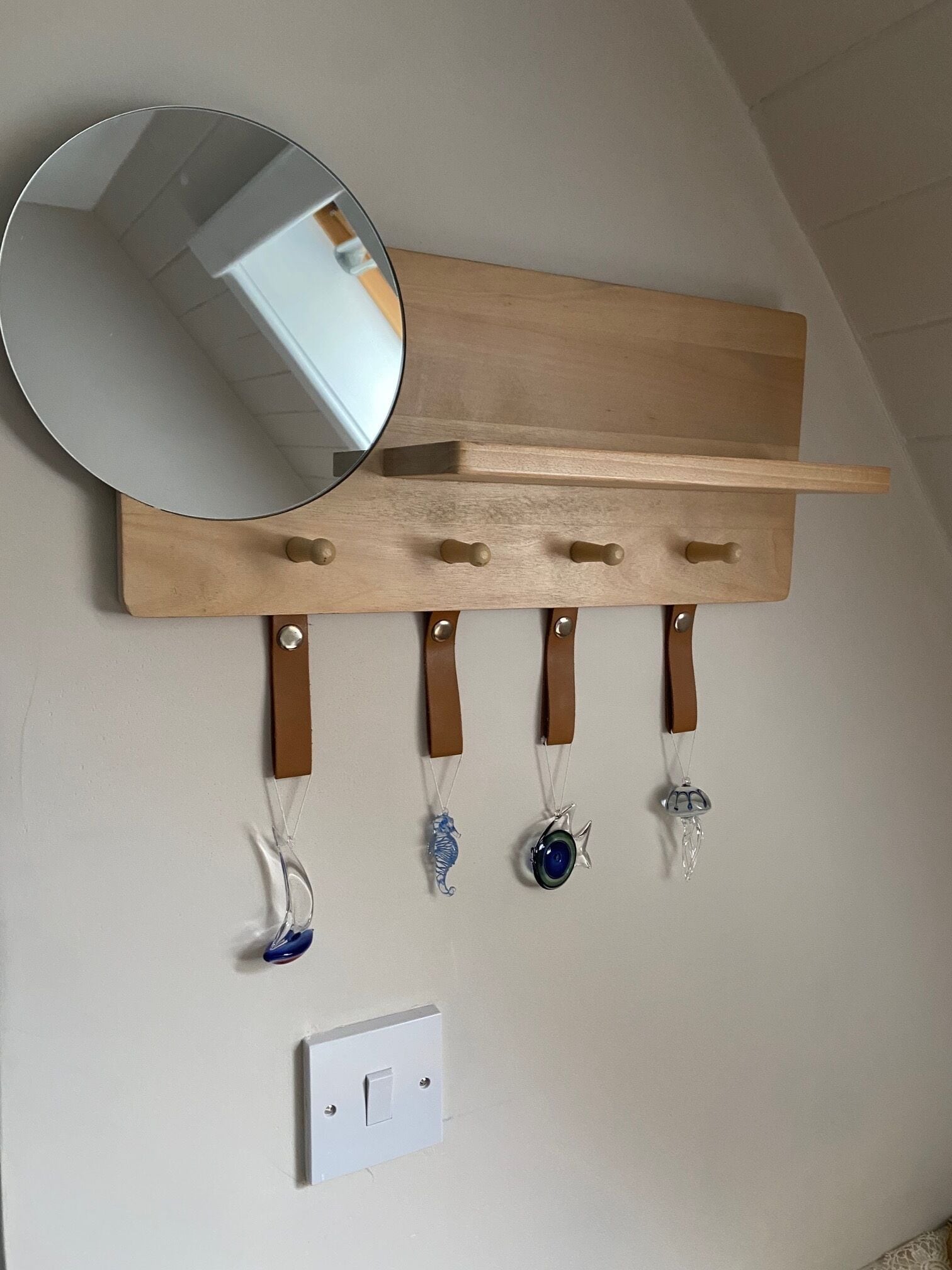 Un porte-objets en bois, fixé au mur, muni de crochets sur lesquels sont suspendus divers ornements en verre.