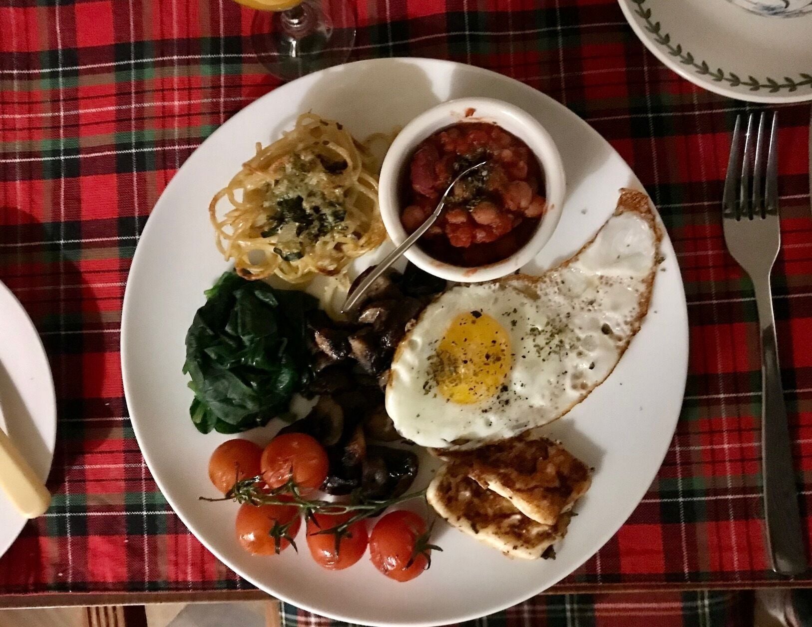 A plate of food with pasta, a fried egg, mushrooms, spinach, and cherry tomatoes.