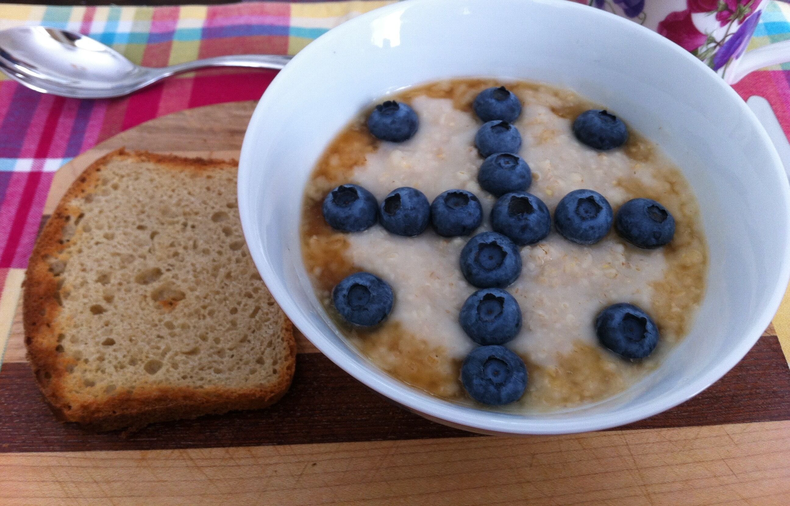 Un tazón de avena con arándanos y una rebanada de pan sobre una tabla de madera.