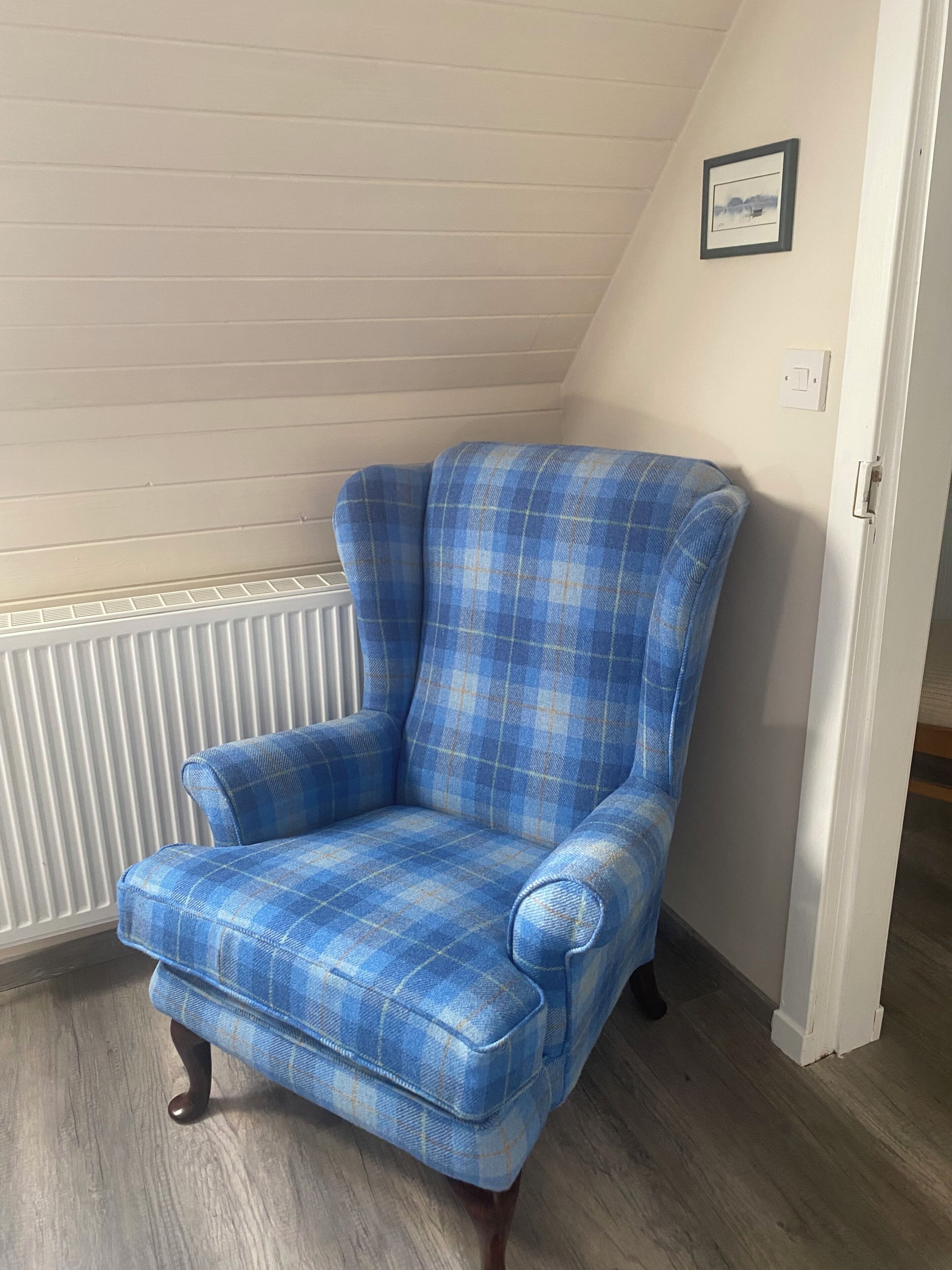 A blue plaid armchair in a room with a sloped ceiling and a white radiator.
