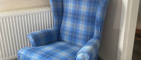 A blue plaid armchair in a room with a sloped ceiling and a white radiator.