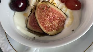 Un tazón blanco con asa que contiene higos, cerezas y uvas sobre un mantel estampado.