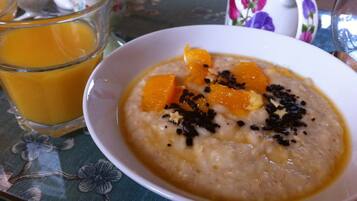 A bowl of oatmeal with orange pieces and black seeds, a glass of orange juice, and a floral mug on a table.
