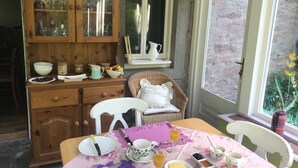 Un coin repas avec un buffet en bois, des chaises en osier et une table dressée avec des assiettes, des tasses et une nappe à motifs floraux.