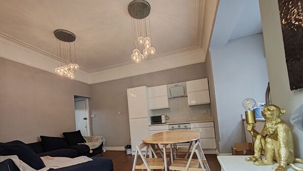 Un salon moderne avec un canapé bleu, une table à manger en bois et un coin cuisine doté de meubles blancs et d’un four à micro-ondes.