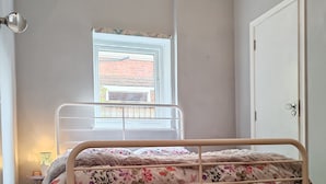 Une chambre à coucher avec un lit, une fenêtre, une porte et une table de chevet avec une lampe.