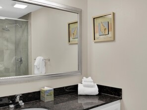 A bathroom with a large mirror, a sink, a towel rack, and two framed artworks on the wall.